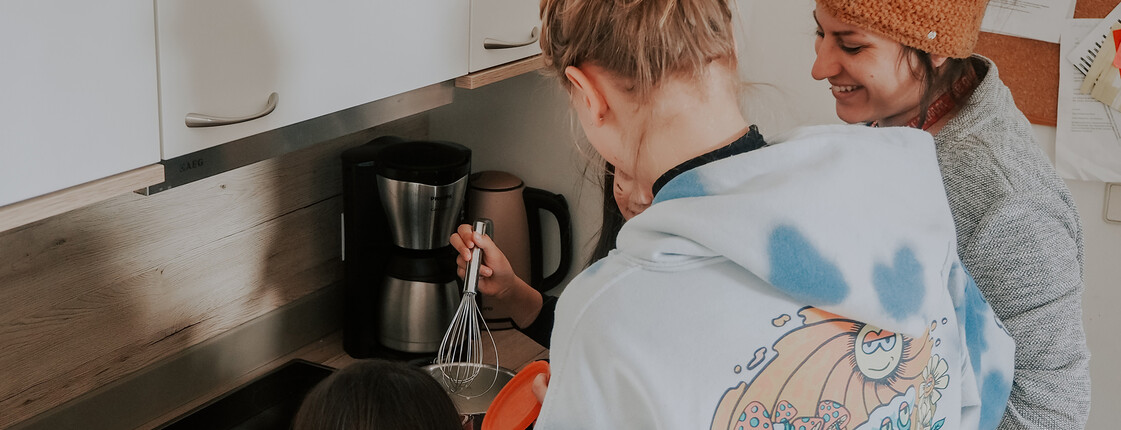 Eine Betreuerin unserer sozialpädagogischen Einrichtung, Haus Antonius in Treffen, kocht mit einer Jugendlichen und einem Mädchen in der Küche einer Wohngruppe.