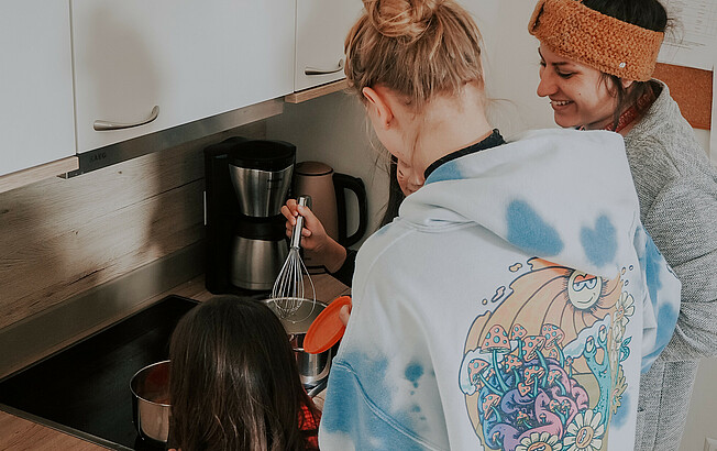 Eine Betreuerin unserer sozialpädagogischen Einrichtung, Haus Antonius in Treffen, kocht mit einer Jugendlichen und einem Mädchen in der Küche einer Wohngruppe.